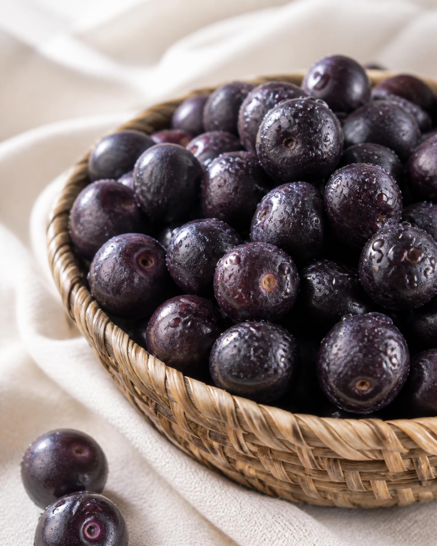 Fresh açaí berries in a woven basket on natural linen